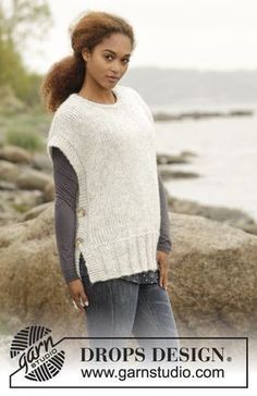 a woman standing in front of rocks wearing a white sweater with buttons on the back