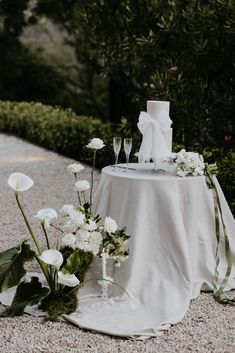 a table topped with white flowers and two wine glasses next to a cake on top of a table