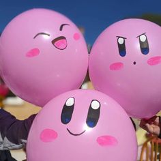 three pink balloons with faces drawn on them are being held by a woman in a black jacket