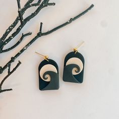 two black and white earrings sitting on top of a table next to some tree branches