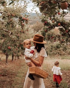 a woman holding a baby in an apple orchard