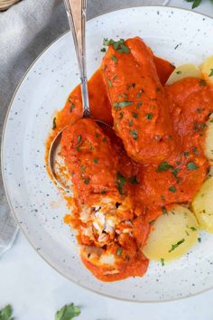 a white plate topped with meat covered in marinara sauce, potatoes and parsley