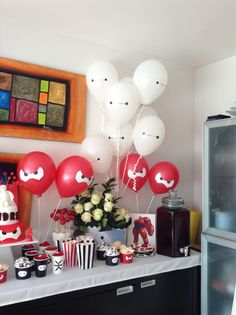 a party with balloons, cake and cupcakes on a table in front of a refrigerator