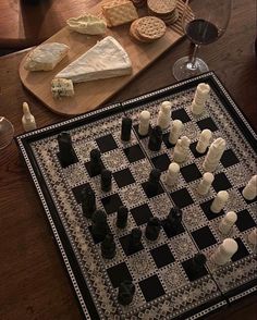 a chess board with cheese and crackers on it next to a glass of wine