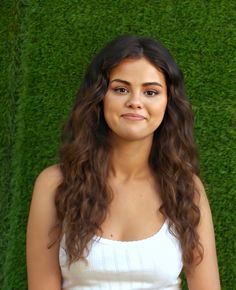 a young woman standing in front of a green grass wall with her hands on her hips