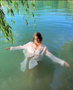 a woman is floating in the water with her arms spread out and she is wearing a white shirt