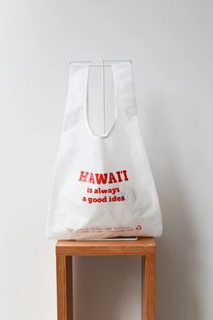 a white shopping bag sitting on top of a wooden stool with the words hawaii is always a good idea