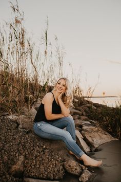 a pregnant woman sitting on rocks near the water at sunset with her hands under her chin