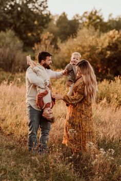 a man and woman are holding their child in the air as they walk through tall grass