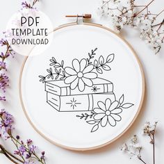 a cross stitch pattern with flowers on it and a book in the middle, surrounded by purple flowers