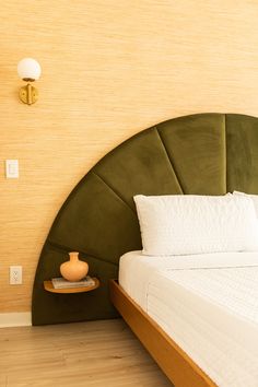 a bed with a green headboard and white pillows in a room that has wood flooring