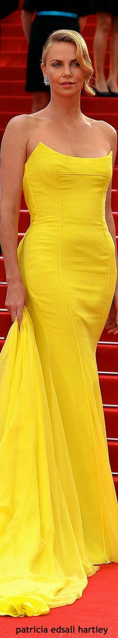 a woman in a yellow dress standing on the red carpet with her hands behind her back