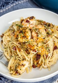 a white bowl filled with pasta and shrimp on top of a blue table cloth next to a fork