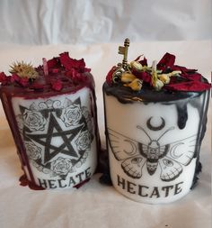 two decorated candles sitting next to each other on a white sheet covered tablecloth with red flowers