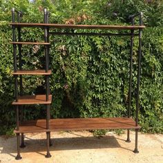 an iron and wood shelving unit in front of a bush