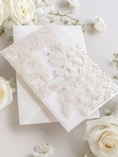 a white wedding card with lace and flowers on the table next to it is an envelope that has been cut in half