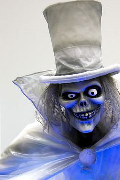 a skeleton wearing a white top hat and blue cape with eyes painted on it's face