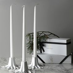 three white candles sitting on top of a table next to a box and christmas tree