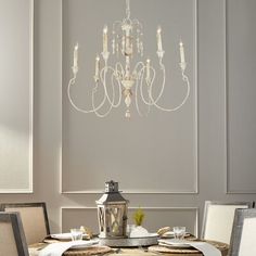 a chandelier hanging from the ceiling over a table with place settings on it