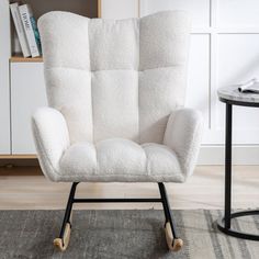 a white chair sitting on top of a rug next to a table and bookshelf