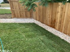 a wooden fence next to a lush green yard with rocks and grass on the ground