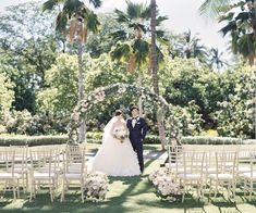 a bride and groom standing in front of an arch with white flowers on the grass