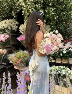 a woman in a blue dress is looking at flowers and holding her hands behind her head