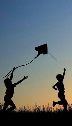 two children are flying a kite in the sky at sunset or dawn with their hands up