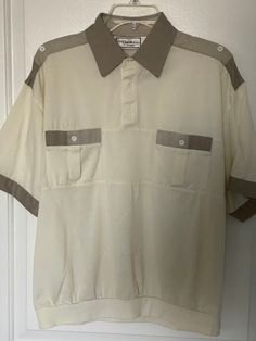 Really nice example of an 80s sport shirt with elastic waist by "Classics by Palmland" Shirt is a taupe/light grey with darker grey/toupe solid and striped accents ok the pockets, collar, sleeves and tops of shoulders. Three button placard, Pointed collar, Two button closure breast pockets, elastic waist band, shirt sleeves. One button adorns each shoulder. Shirt is labeled a large, 22" across chest but allows stretch due to elastic waist. Casual Beige Polo Shirt With Ribbed Collar, Casual Cream Polo Shirt With Ribbed Collar, Retro White Top With Ribbed Collar, White Retro Top With Ribbed Collar, Casual Cream Collared Tops, Cream Polo Collar Top With Ribbed Details, Retro Relaxed Fit Polo Collar Top, Retro Relaxed Fit Top With Polo Collar, Retro Top With Relaxed Fit And Polo Collar