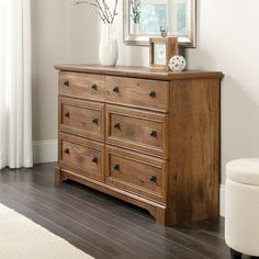 a wooden dresser sitting next to a window with a vase on top of it and a mirror above it