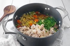 a pot filled with meat and vegetables on top of a white tablecloth next to a wooden spoon