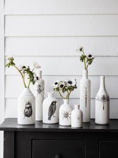 several white vases with flowers in them sitting on a black table next to a wall