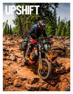 a man riding on the back of a dirt bike down a rocky slope with trees in the background