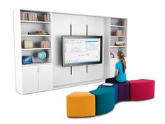 a woman sitting in front of a flat screen tv next to colorful stools and bookshelves