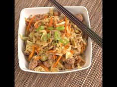 a white bowl filled with meat and vegetables next to chopsticks on a table