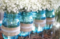 white flowers are in blue mason jars with burlocks and twine on them