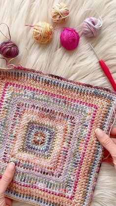 two hands are holding a crocheted bag with balls of yarn in the background