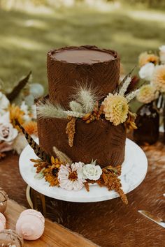 a three tiered chocolate cake on a table with flowers and feathers around the edges