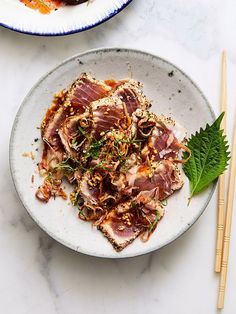 a white plate topped with meat and vegetables next to chopsticks