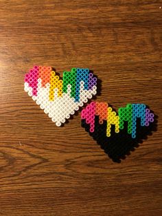 two heart shaped pieces made out of perler beads on a wooden surface with the word love spelled in multicolored letters