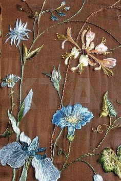 an embroidered fabric with blue flowers and green leaves on brown background, close - up