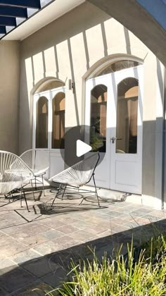 two white chairs sitting on top of a patio next to a building with arched windows