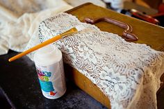 an old suitcase is sitting on a table with a crochet doily and paintbrush