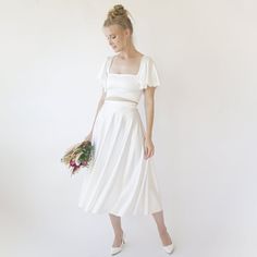 a woman in a white dress is holding a bouquet and looking down at the ground