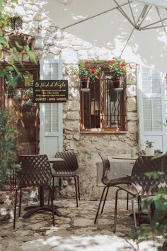 an outdoor cafe with tables, chairs and umbrellas in front of the building's windows