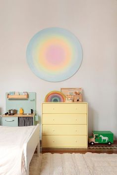 a child's bedroom with a dresser, toy cars and a painting on the wall