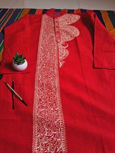 a red shirt with white designs on it next to a potted plant and pencil