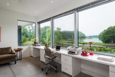 a home office with large windows overlooking a lake and trees in the distance is shown