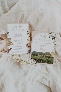 the wedding stationery is laid out on a bed with white linens and flowers