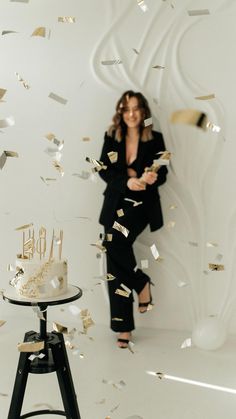 a woman standing in front of a cake with gold confetti falling from it